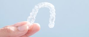 Image of a hand holding clear aligners like Invisalign.