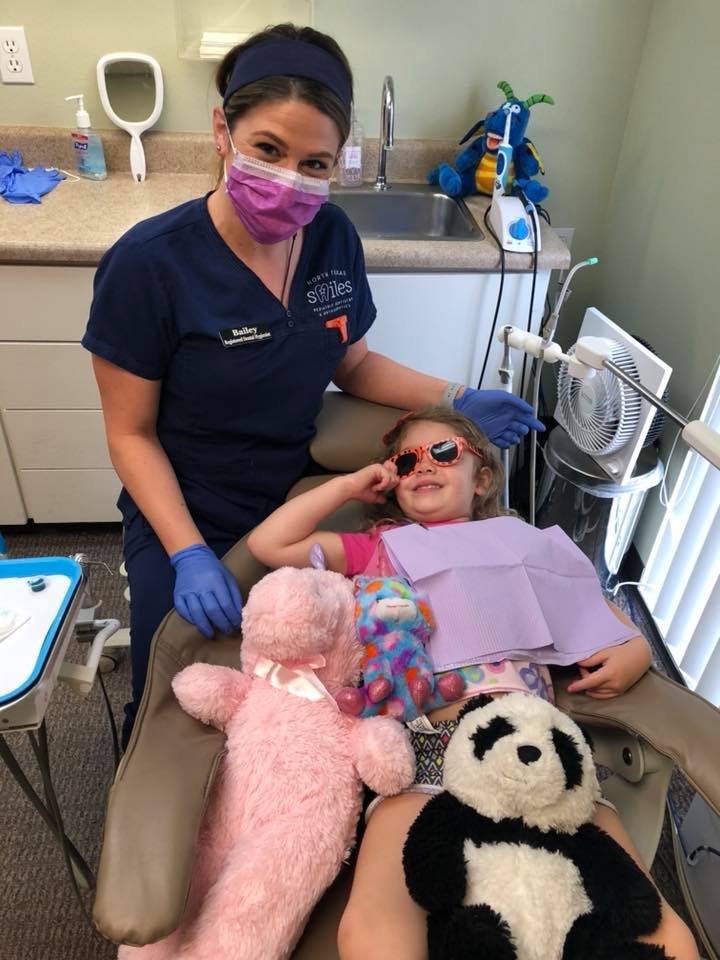Image of a young girl taking advantage of pediatric dentistry services with stuffed animals to help make her feel more comfortable and enjoy her time at the dentist. 